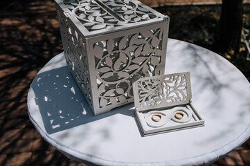 A white wooden rectangular box with a pattern, an infinity symbol with gold rings lies on a white...