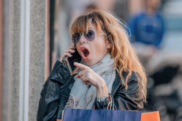 Fototapeta premium middle-aged woman in the street with shopping bags and mobile phone with a surprised expression