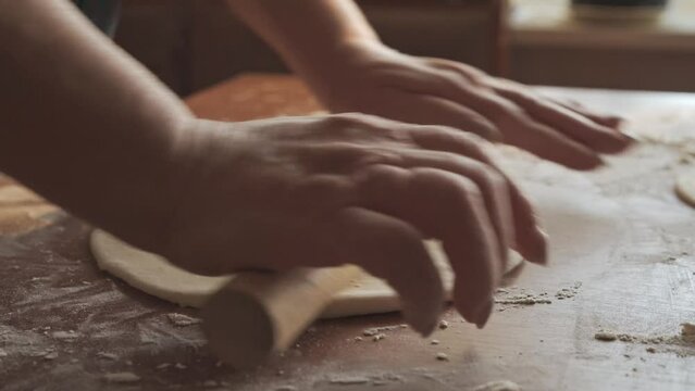 Women's hands, using a rolling pin, roll out the dough for baking. Homemade simple kitchen in the countryside.