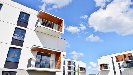 Part of a white residential building  with balconies and blue sky with clouds. Architectural details in modern apartment building on a sunny day.