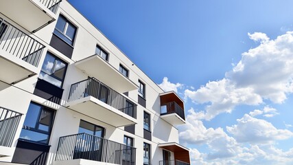 Part of a white residential building  with balconies and blue sky with clouds. Architectural details in modern apartment building on a sunny day.