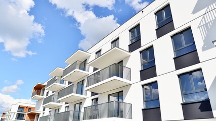 Part of a white residential building  with balconies and blue sky with clouds. Architectural details in modern apartment building on a sunny day. - obrazy, fototapety, plakaty