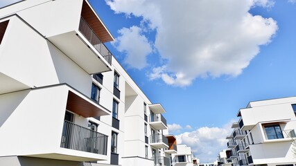Part of a white residential building  with balconies and blue sky with clouds. Architectural details in modern apartment building on a sunny day.