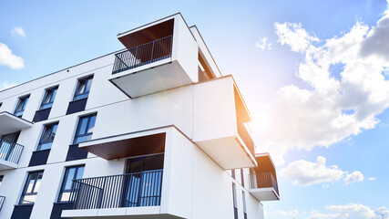 Part of a white residential building  with balconies and blue sky with clouds. Architectural details in modern apartment building on a sunny day.