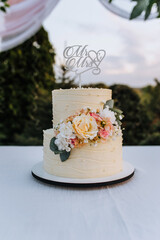 A beautiful round two-tier wedding cake with the word Mr and Mrs, decorated with flowers, roses, stands on a table with a white tablecloth. Food photography.