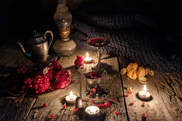 Pomegranate seeds and pomegranate wine next to silverware. Dark vintage photo with rough wood background and candles.