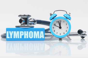 On a white surface there is an alarm clock, a stethoscope and a blue block with the inscription - LYMPHOMA