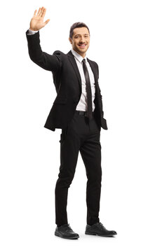 Full length shot of a young man in a black suit and tie smiling and waving