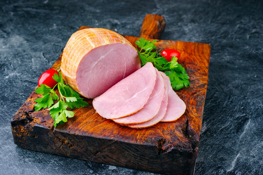 Traditional German boiled Easter ham with tomatoes and parsley offered as close-up on an old rustic wooden board with copy space