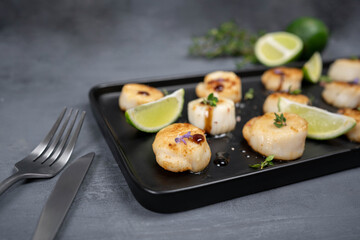 Fried scallops with butter lemon spicy sauce on black plate over old dark stone background.