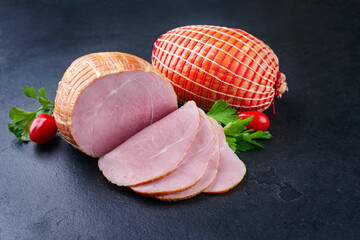 Traditional German boiled Easter ham with tomatoes and parsley offered as close-up on a black board...