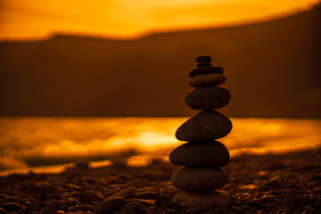 Pebble pyramid silhouette on the beach. Sunset with sea in the background. Zen stones on the sea beach concept, tranquility, balance. Selective focus