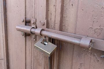 Padlock on a metal latch. The wooden gates are locked. Concept of locked entry and security. New closed padlock on the pin of a rustic wooden door.