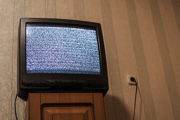 Retro old tube television with static glitch displayed on screen standing on wooden nightstand at...