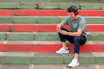 Latin man sitting on colorful stairs typical of Latin America, looking at his cell phone and...