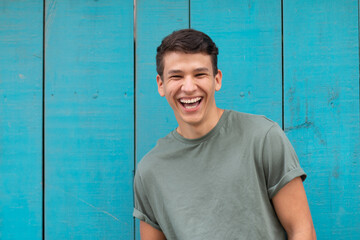 Obraz premium Young latin with an authentic laugh, in the background a blue door typical of latin homes. Latin representation in a portrait.