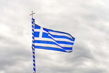 The national flag of Greece looks like 9 white and blue stripes with a cross on a background of a gray cloudy sky. close up