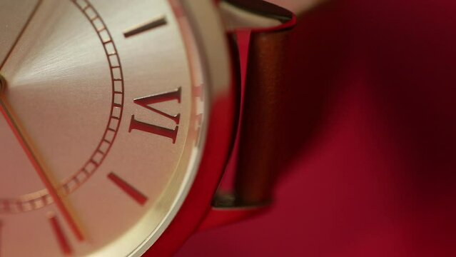 Extreme closeup of gold metallic second arrow passing by on  clock face. Red background for copy space. macro watch.