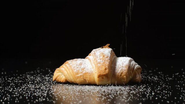 Powdered sugar sprinkling onto a croissant.