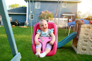 Fototapeta na wymiar Beautiful blonde smiling girl is swinging outside on a summer day.