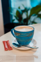 A cup of cappuccino on a saucer stands in a cafe on a table near the window