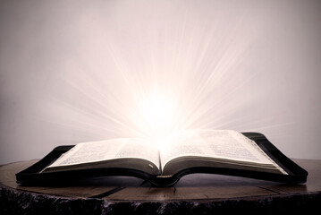 Open Bible. The big book of the Bible lies on a wooden table. In the dark. A light shines on the...