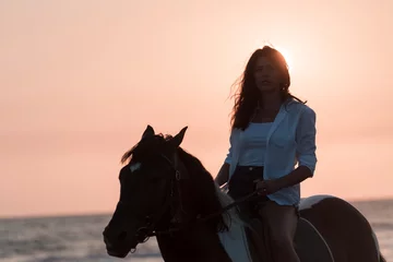 Fotobehang Woman in summer clothes enjoys riding a horse on a beautiful sandy beach at sunset. Selective focus  © .shock