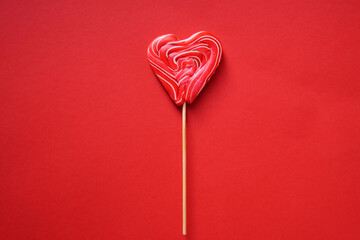 A red multi-colored lollipop in the shape of a heart. On a red background.