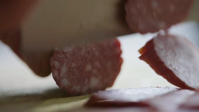 Close up shot of male hands slicing salami sausage with knife