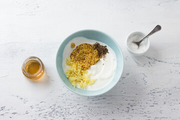 Preparation of salad yogurt dressing with ginger, mustard, black pepper, salt and wine vinegar in a blue ceramic bowl on a light gray background. Cooking healthy homemade food