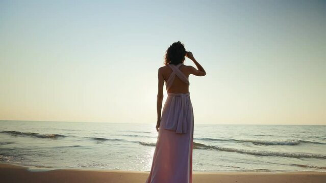 Woman holds and lets go of her dress against sunset sea background