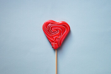 Red multi-colored lollipop in the form of a heart. Blue background.