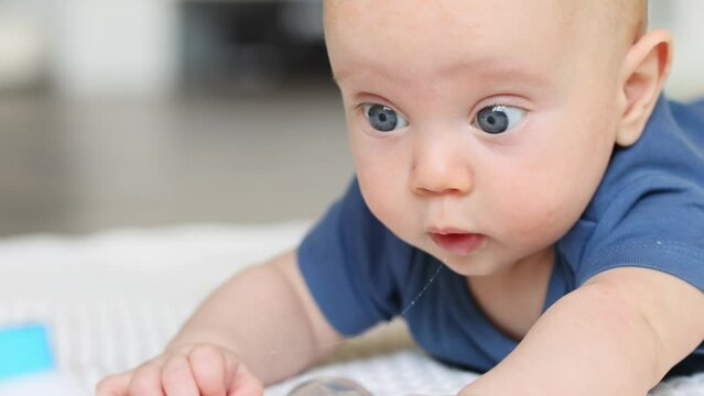 4 months baby infant lying on stomach on floor in living room, trying to crawl to reach colorful toy. caucasian blue eyed child adorable face, positive emotions, activity indoors. 