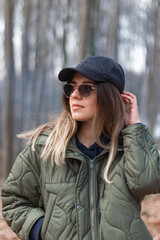 Happy, smiling, young girl with hat and sun glasses in forest. Fresh air and nature admiration concept. Blur trees background. 