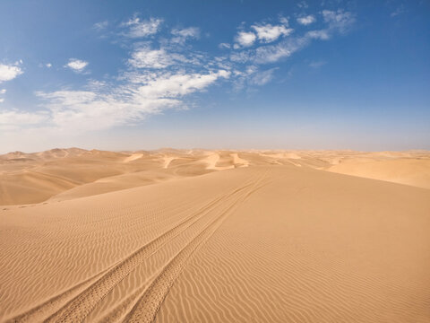 Big sand dunes in the middle of the desert near Swakopmund, Namibia, with tracks of a quad bike cutting through the otherwise perfectly, wind-made pattern in the sand. © Philipp