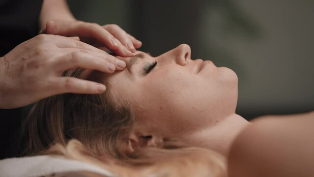 chiropractor is massaging acupuncture points on face of woman for relaxing and curing headache