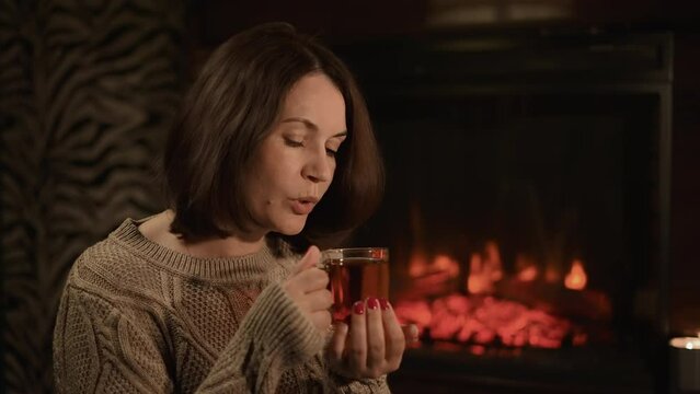 A beautiful brunette cools tea by the fireplace in the evening