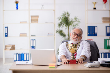 Old male employee being awarded with golden cup