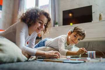 small boy and girl drawing on the green board at home two children brother and sister siblings or friends lying on the floor using chalk leisure and education real people family concept copy space