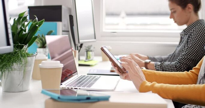 Diverse group of businesspeople sitting at their desks typing on computer keyboards and. sending text messages on cellphones. Professional corporate team working on tech devices at their desk in a row