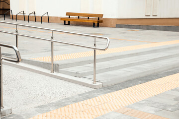 Outdoor stairs with ramp, metal railing and tactile tiles. Public environment accessibility