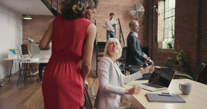 A businesswoman helping a group of diverse team members in her office. Happy businesswoman walking through her office talking to staff. Young Hispanic boss collaborating with colleagues in the office