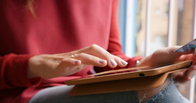 Closeup of the hand of a woman using her wireless tablet, paying for online shopping purchases with her credit card. A woman browsing through a digital app on her wireless tablet. Woman at home