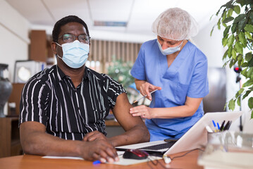 Fototapeta na wymiar African american office employee in protective face mask getting antiviral injection at workplace. Vaccination, immunization and disease prevention concept