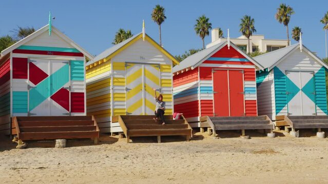 A women sitting on the stairs of a colourful Beach Box, sees someone she knows and waves to them