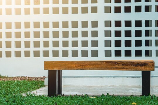 Long wooden chair with white wall background.