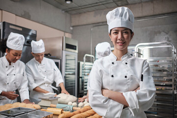 Young beautiful Asian female chef in white cooking uniform looks at camera, arms crossed and...