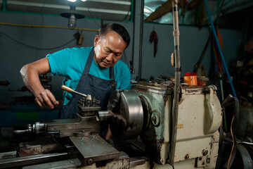 Fototapeta na wymiar A senior craftsman who is skilled in craftsmanship, is controlling, skillfully operating a lathe, is in a small factory that is his family business.