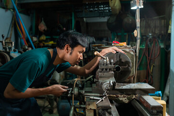  A young Asian craftsman in a small factory, a family business, was standing closely to control the lathe, carefully, and had a serious expression.