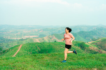 Fototapeta premium Young Asian woman runner, wearing black sportswear, running on a big mountain trail, cool morning, windmills, and sky in the background.